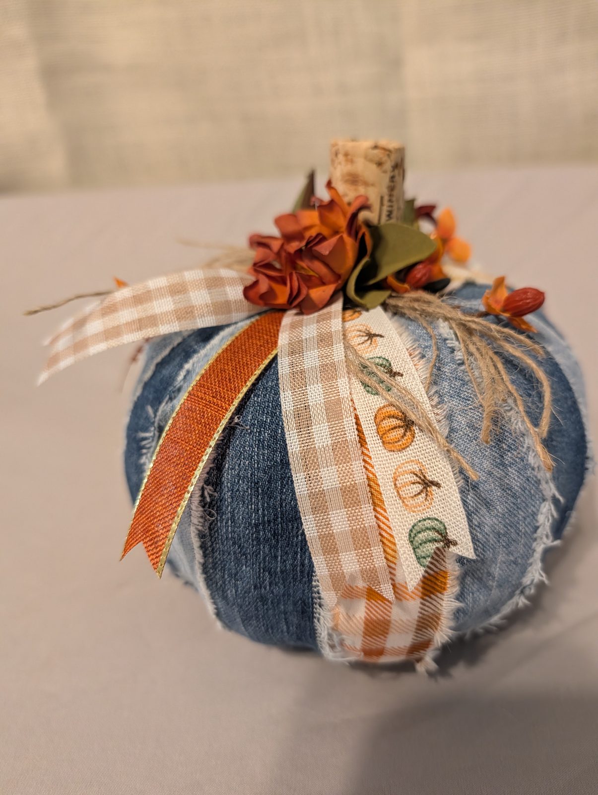 Fabric pumpkin made from frayed denim panels, topped with a cork stem, silk mums and pumpkin-print ribbon