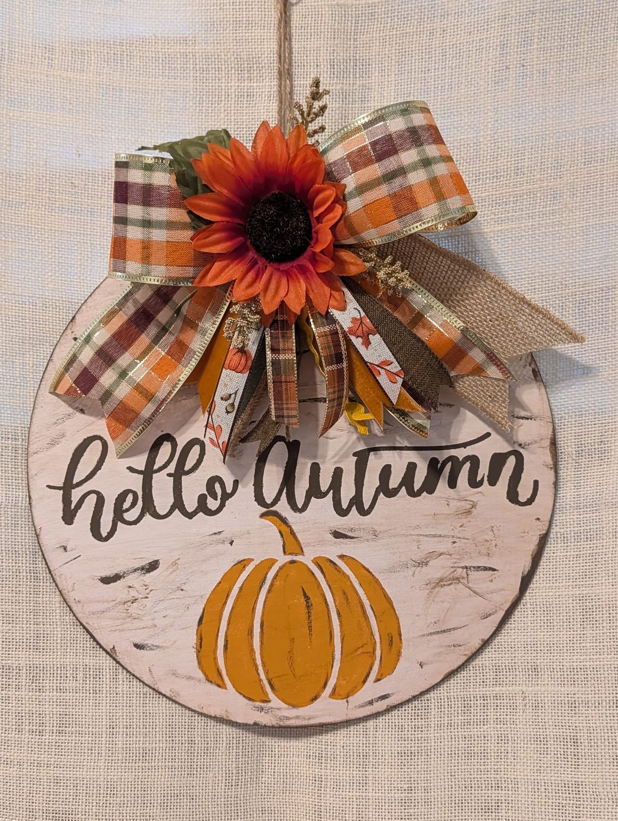 Pumpkin-shaped whitewashed wood sign lettered &lsquo;hello autumn&rsquo; with a plaid ribbon bow