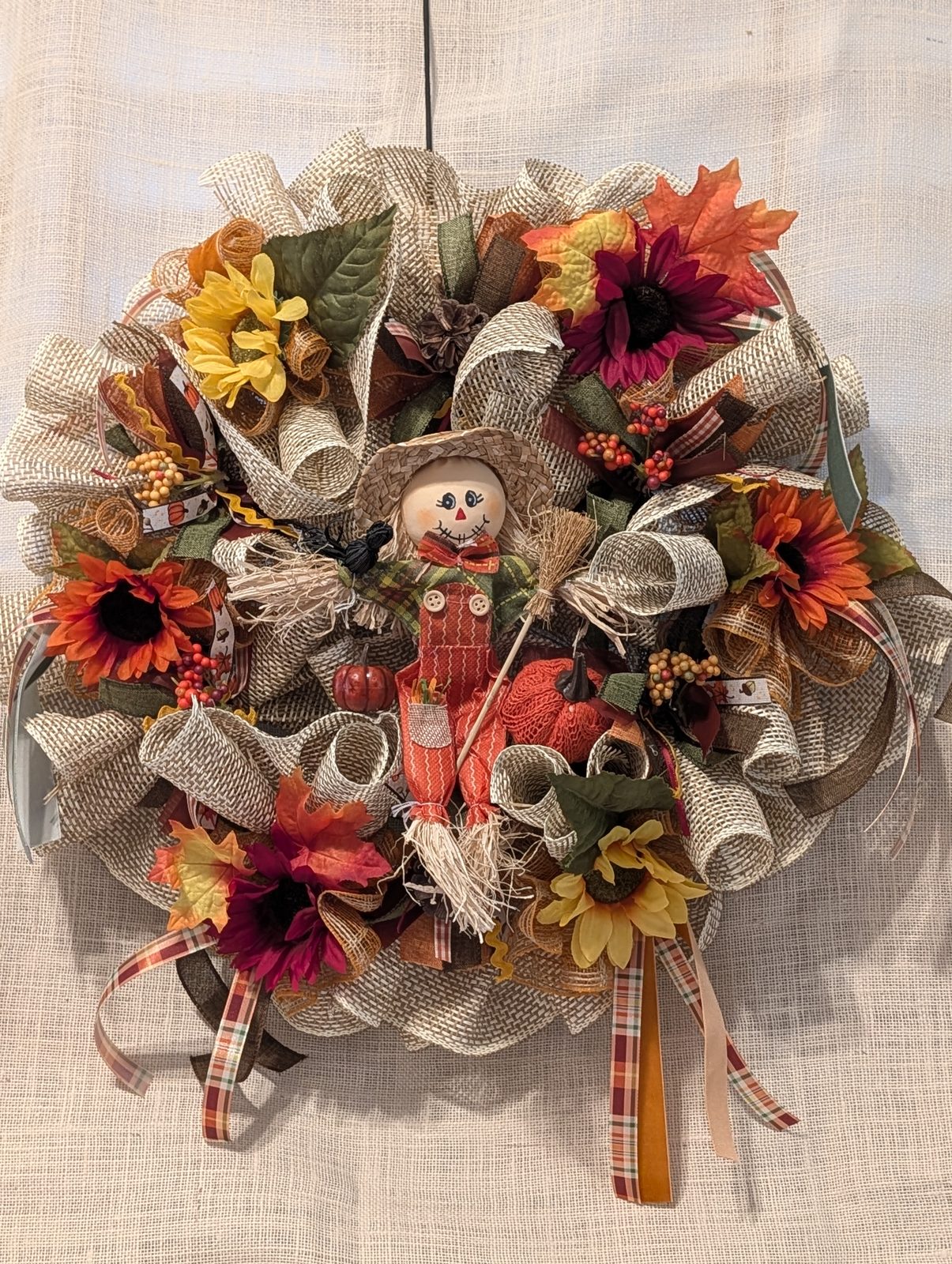 Burlap deco-mesh wreath with a little scarecrow at the center, ringed with sunflowers and maple leaves